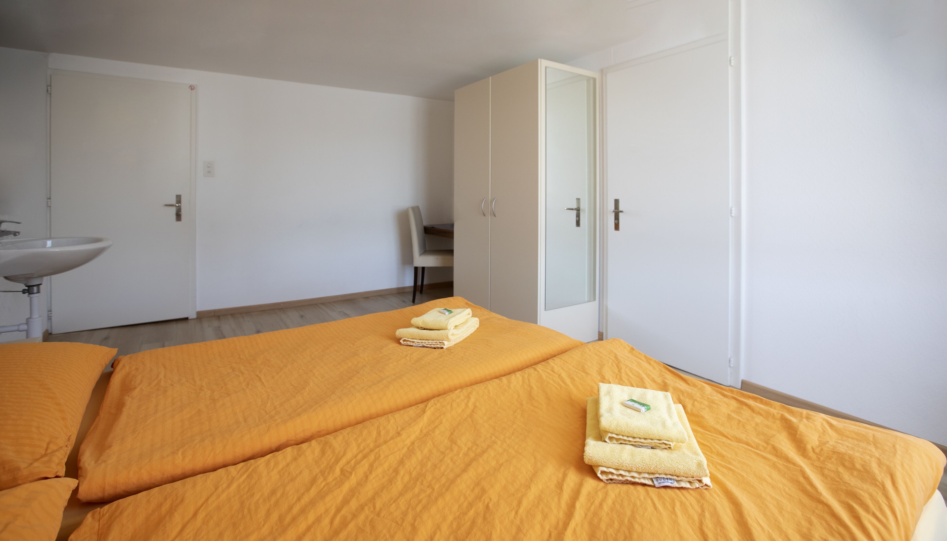 A hotel room with two beds, a bathroom with a sink, and a wardrobe.