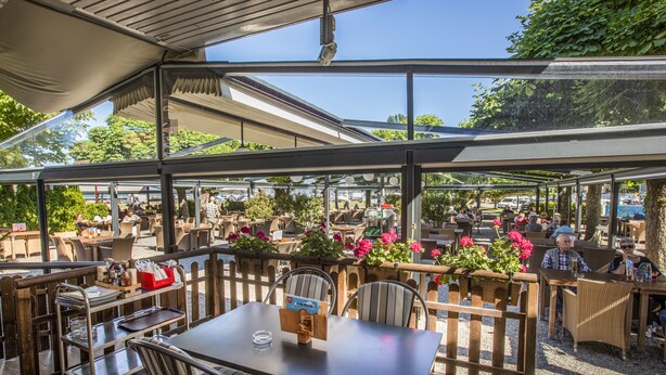 An outdoor café with tables and chairs, a covered seating area, and potted plants. - Hotel Rotes Kreuz (Arbon)