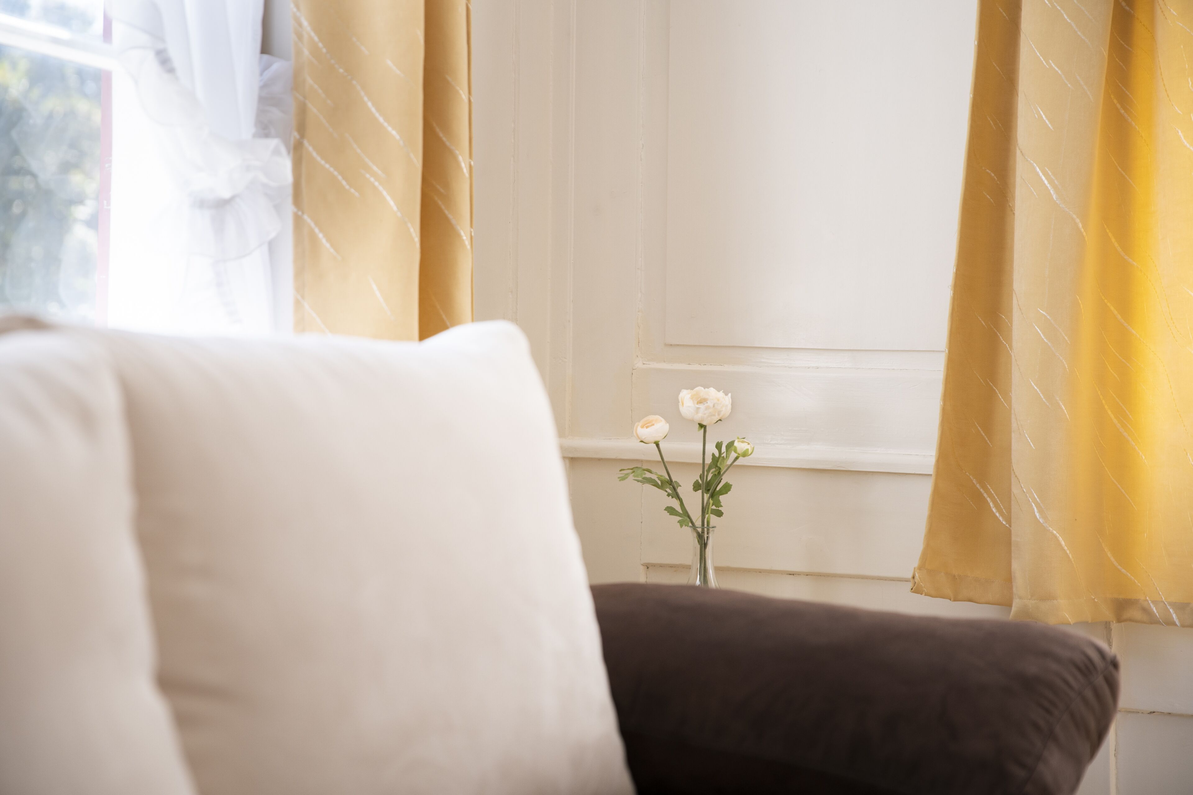 A room with a white wall, a window with yellow curtains, and a brown sofa.