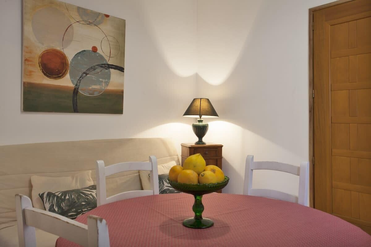 Een eethoek met een ronde tafel, stoelen, een lamp en een schaal met fruit.