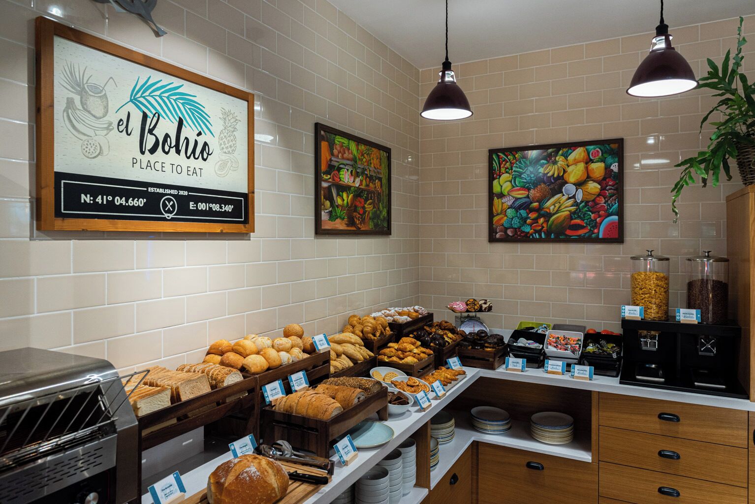 Mostrador de panadería con diversos panes y pasteles, un letrero que dice "el Bolio Place to Eat" y una pintura de frutas en la pared.