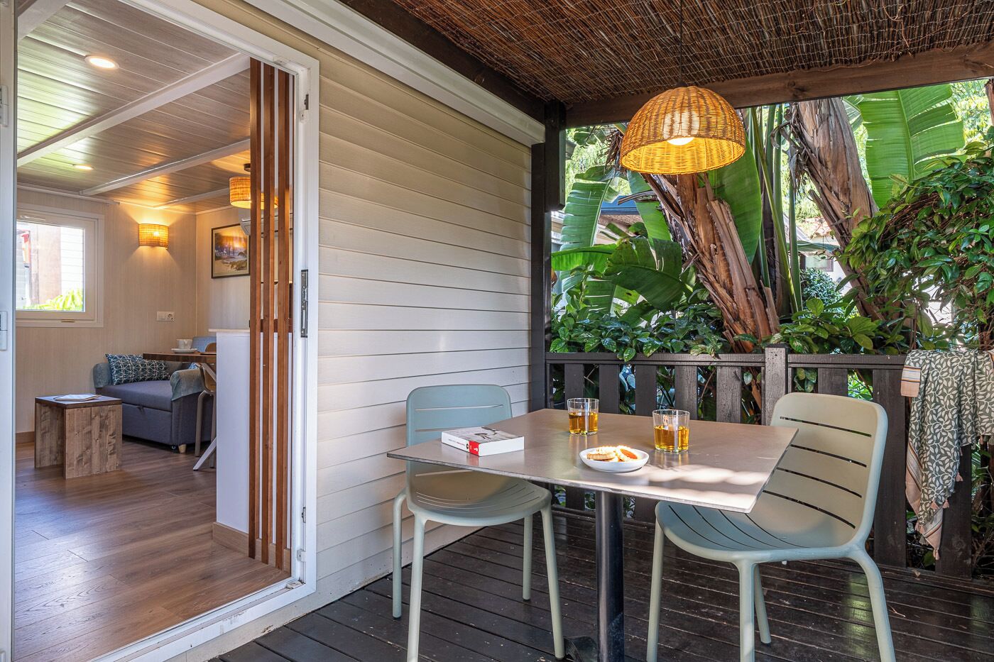Un patio exterior acogedor con una mesa lista para dos personas, rodeado de sillas y un colgante de mimbre sobre él.