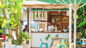 Een bar met een houten toonbank, barstoelen en een groene parasol.
