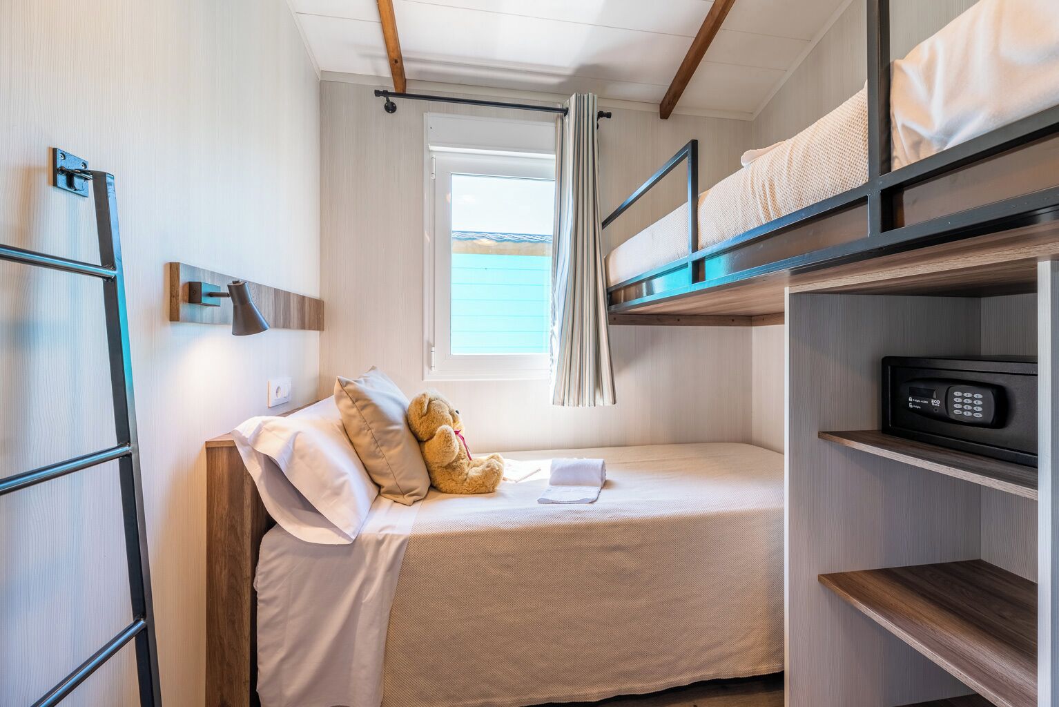 Habitación con literas, una ventana, una mesita de noche con lámpara y un microondas en un estante.