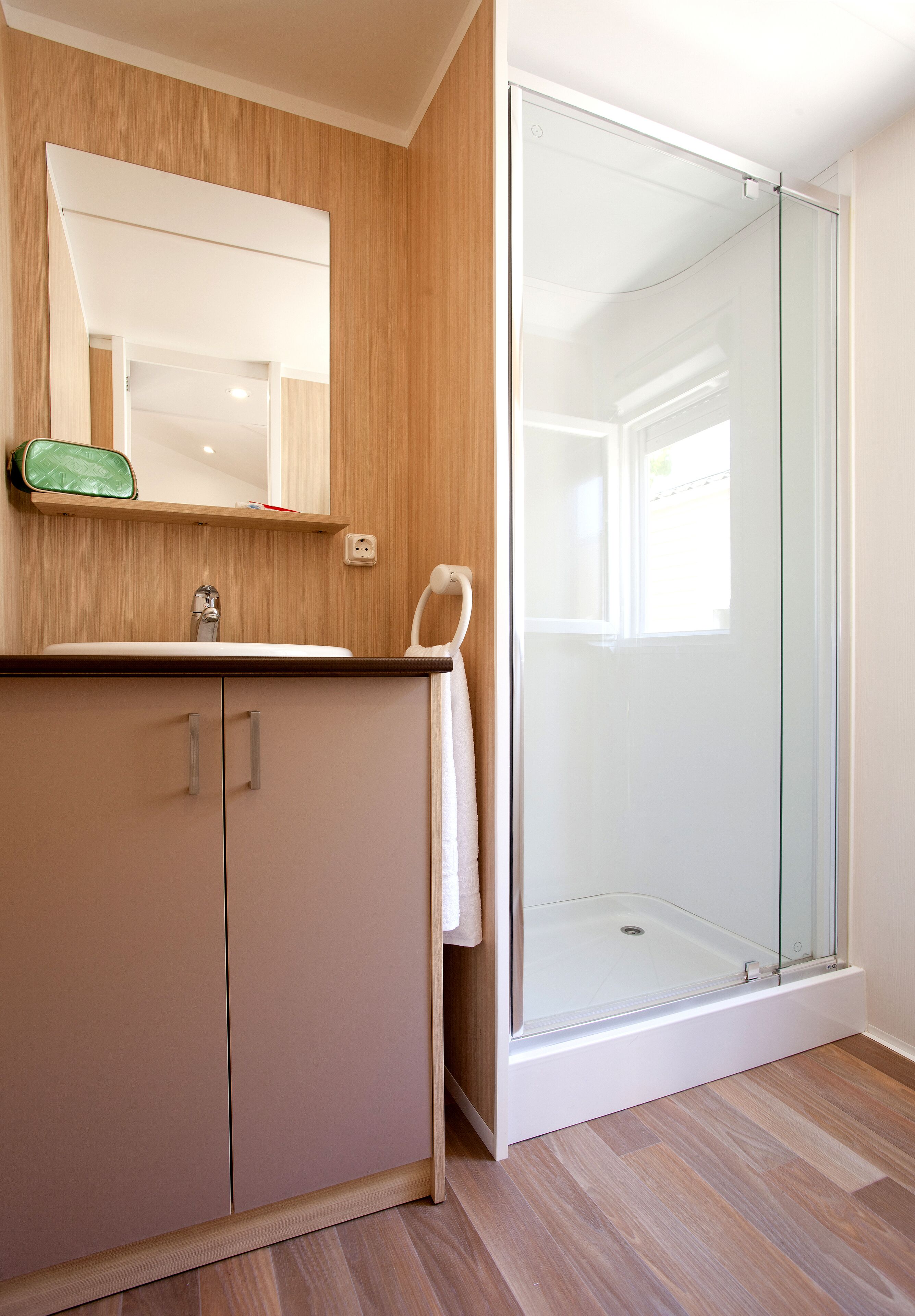 Un bagno moderno con un mobile lavabo in legno, cabina doccia in vetro e specchio sopra il lavandino.