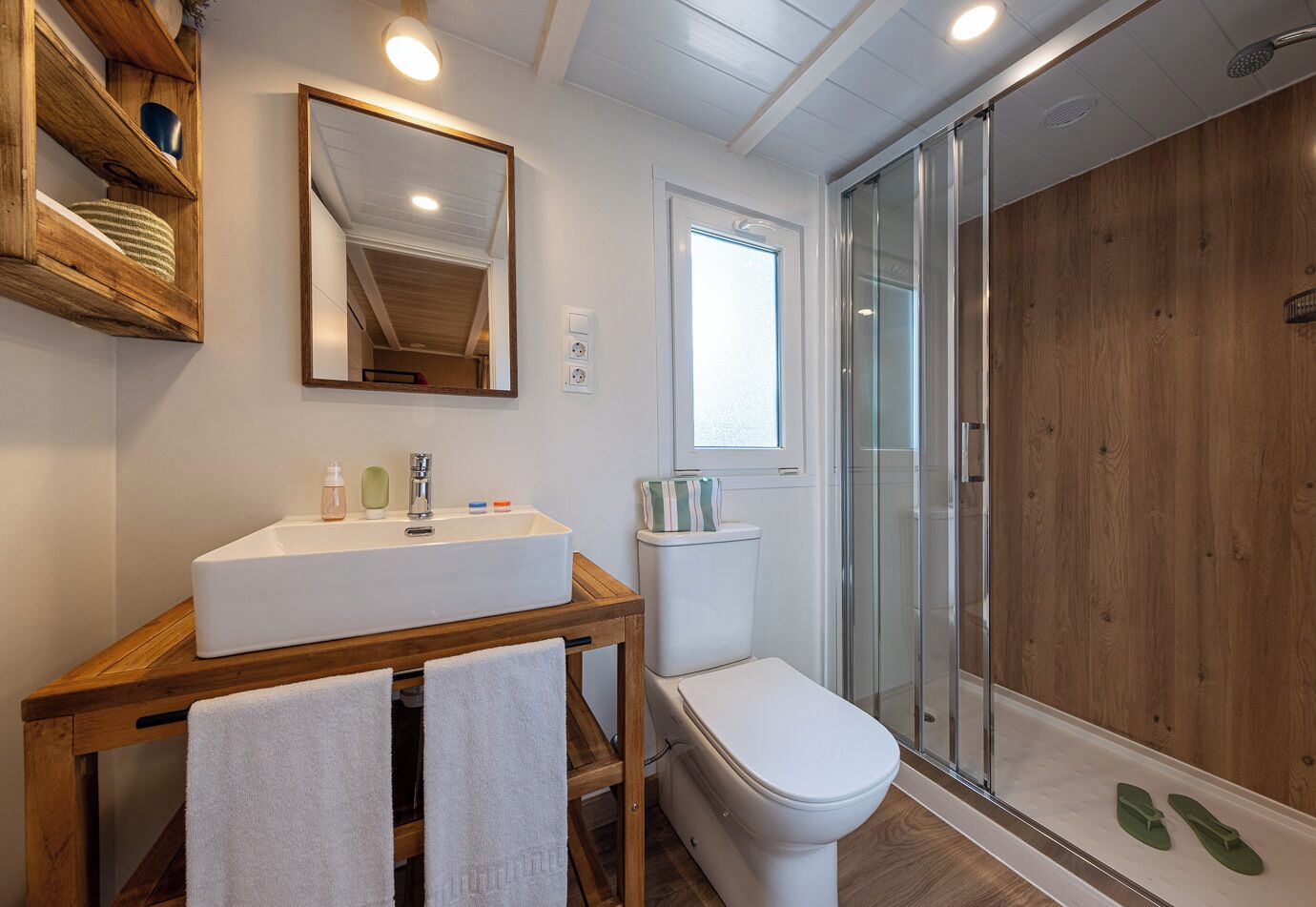 Un baño con tocador de madera, lavamanos blanco y cabina de ducha con mampara de vidrio.
