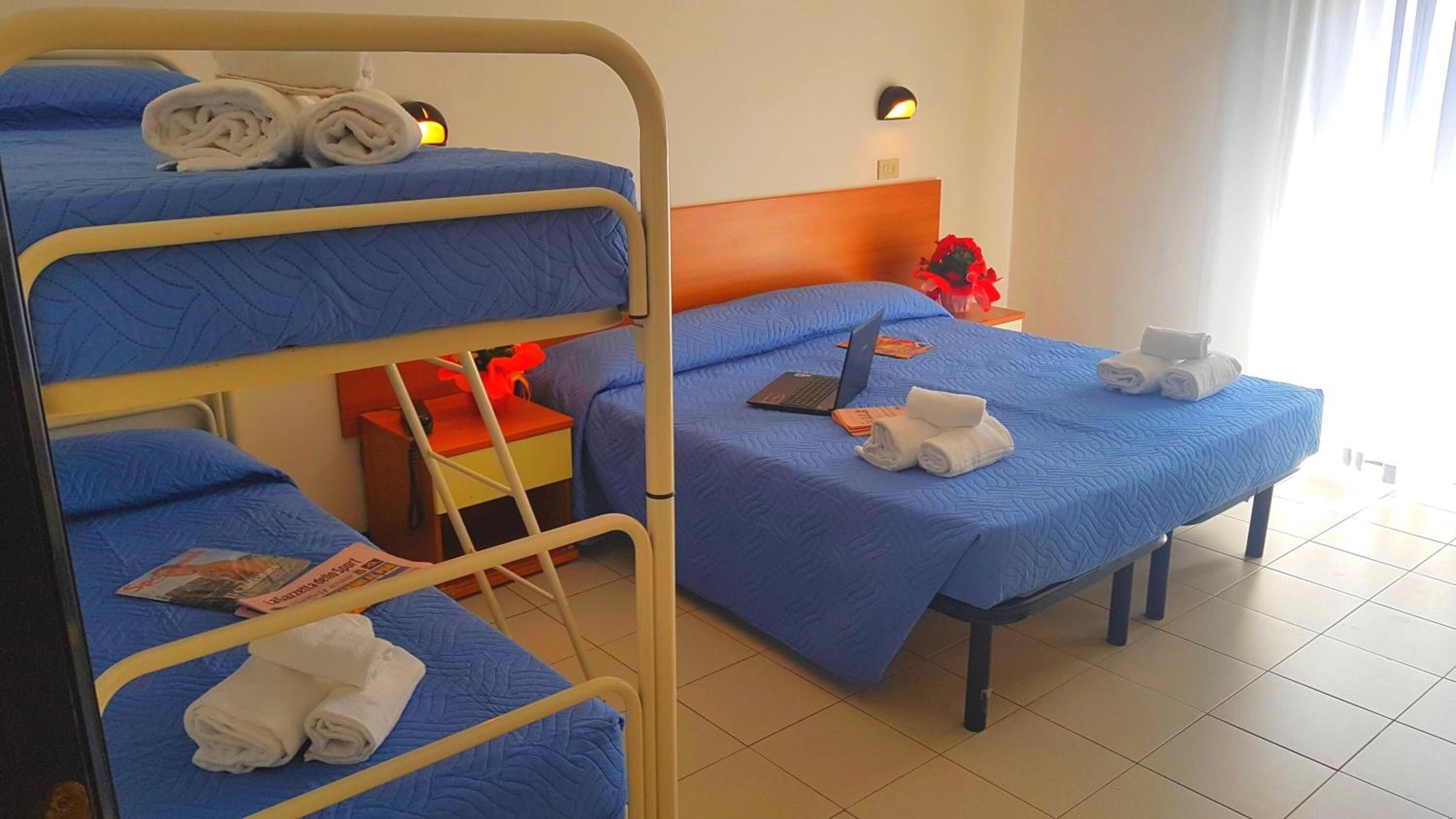 A hotel room with bunk beds, a desk, a chair, a laptop, and towels.