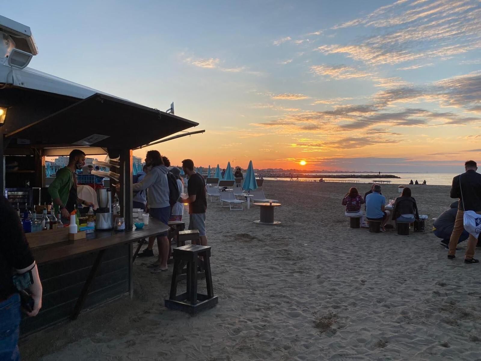 Un bar en la playa con mesas al aire libre y vistas al atardecer.
