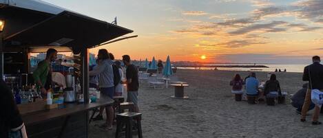 Un bar en la playa con mesas al aire libre y vistas al atardecer.