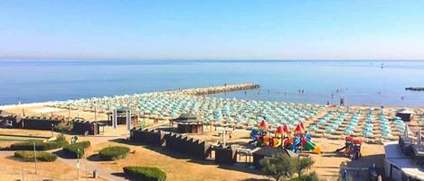 A beach with rows of umbrellas and sun loungers, a pier extending into the water, and a few people in the distance.