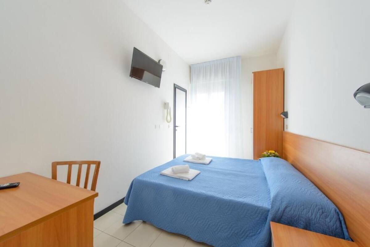 A small, neatly arranged bedroom with a single bed, a wooden desk, and a chair.