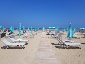 A beach with rows of sun loungers and umbrellas, a wooden walkway leading to the water, and a clear blue sky. - Hotel Paloma (Rimini)