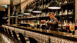 Un espace bar avec un barman préparant des boissons, des étagères remplies de bouteilles d’alcool et des tabourets de bar.