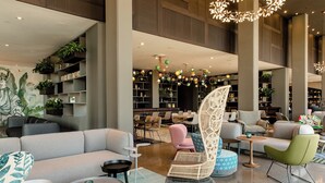 Un hall d’entrée spacieux, doté d’un canapé moderne, d’un fauteuil en osier et d’une table ronde. On y trouve plusieurs coins salon et une grande bibliothèque remplie de livres.