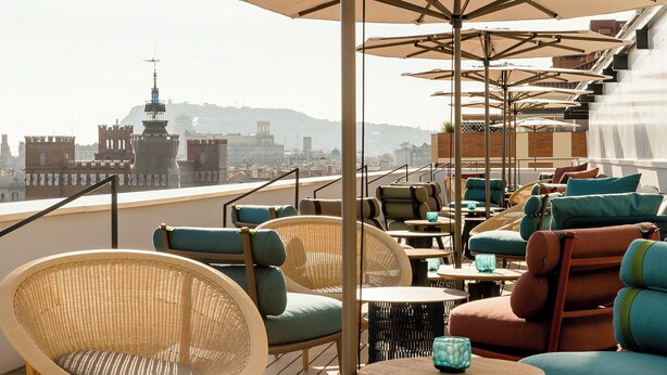 Une terrasse sur le toit, avec des chaises et des tables en osier, des parasols et une vue sur la ville.