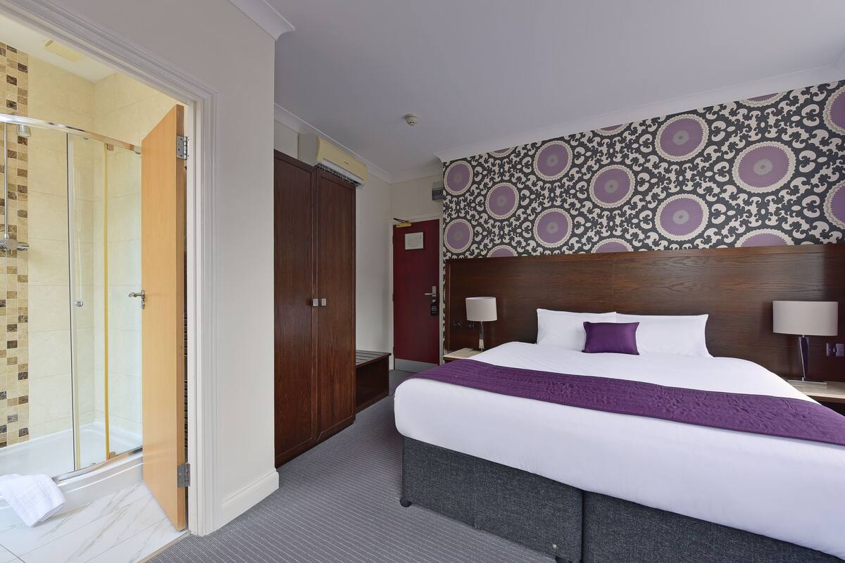 A hotel room with a large bed, a wooden headboard, a shower area, and a patterned wall.
