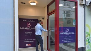 Een man opent een glazen deur naar de receptie van Hotel Bocarddo in Oxford.