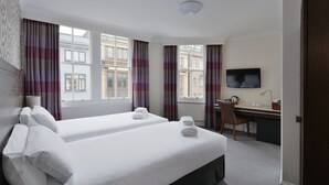 Een hotelkamer met twee bedden, een bureau, een stoel, een televisie en grote ramen met gordijnen.