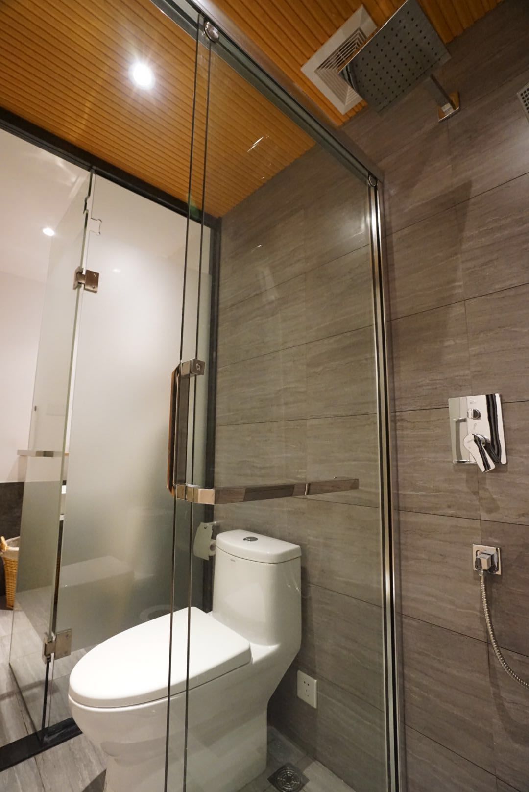 Ein modernes Badezimmer mit Duschkabine aus Glas, einer weißen Toilette und einem an der Wand befestigten Duschkopf.
