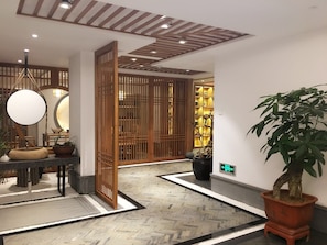 Una hall d'albergo con una reception in legno, un grande specchio, una pianta in vaso e una porta finestra in legno tradizionale.