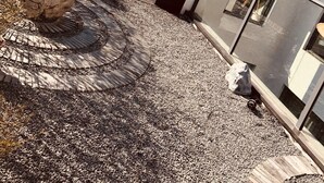 Un edifici modern amb un rètol en una llengua estrangera, una zona d'entrada pavimentada i plantes en testos.