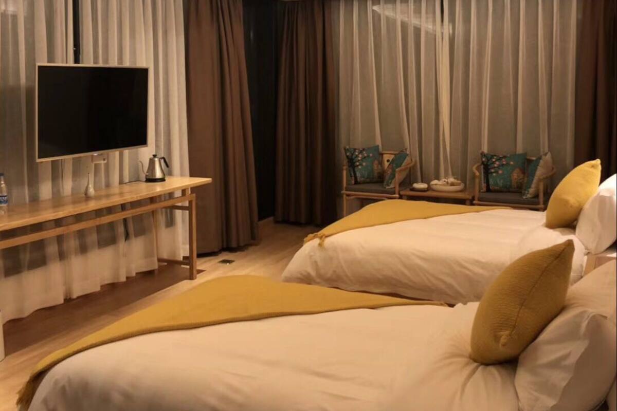 A hotel room with two beds, a TV, a desk with a coffee maker, and a chair.