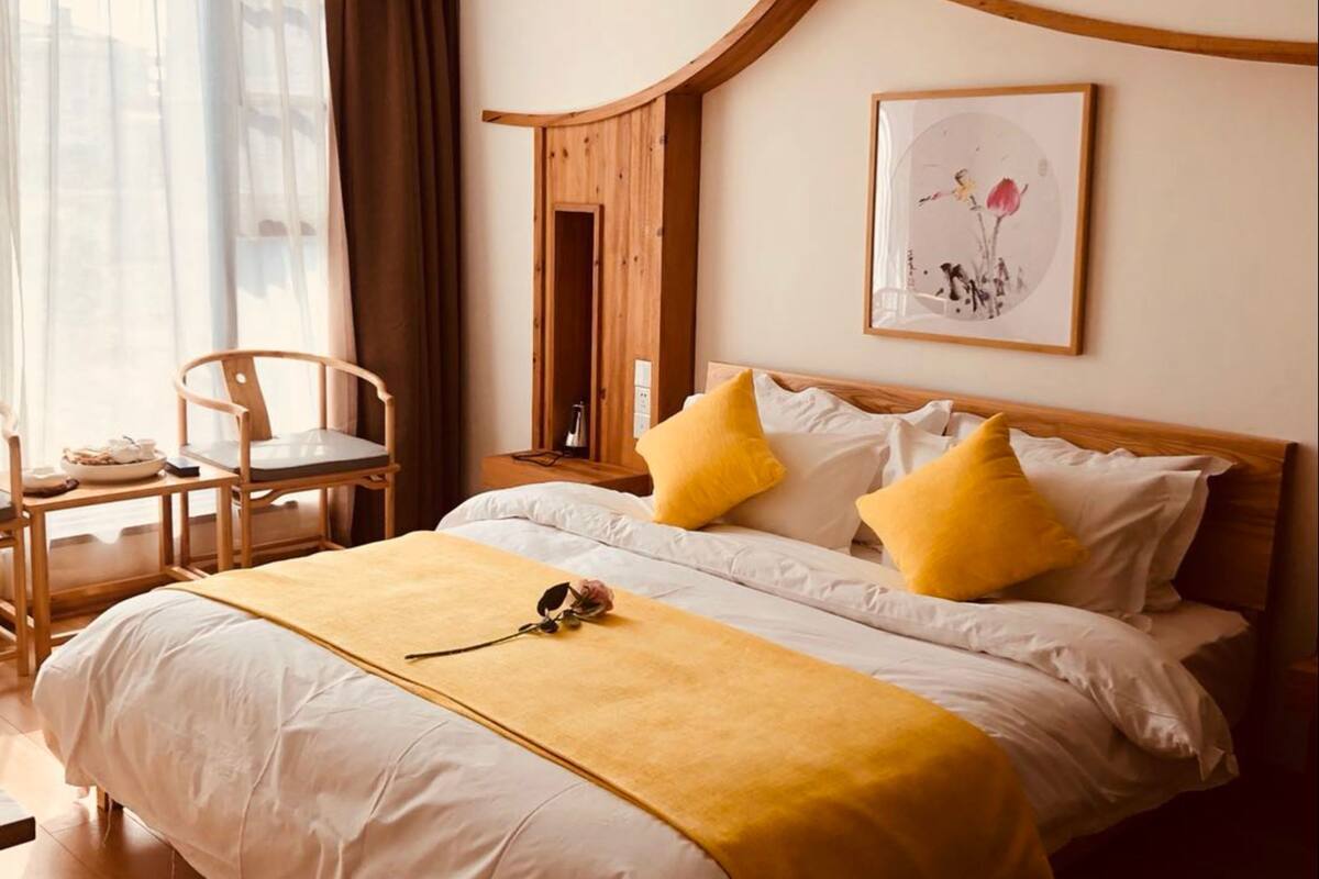 A neatly arranged hotel room with a large bed, a bedside table, a chair, and a window with curtains.