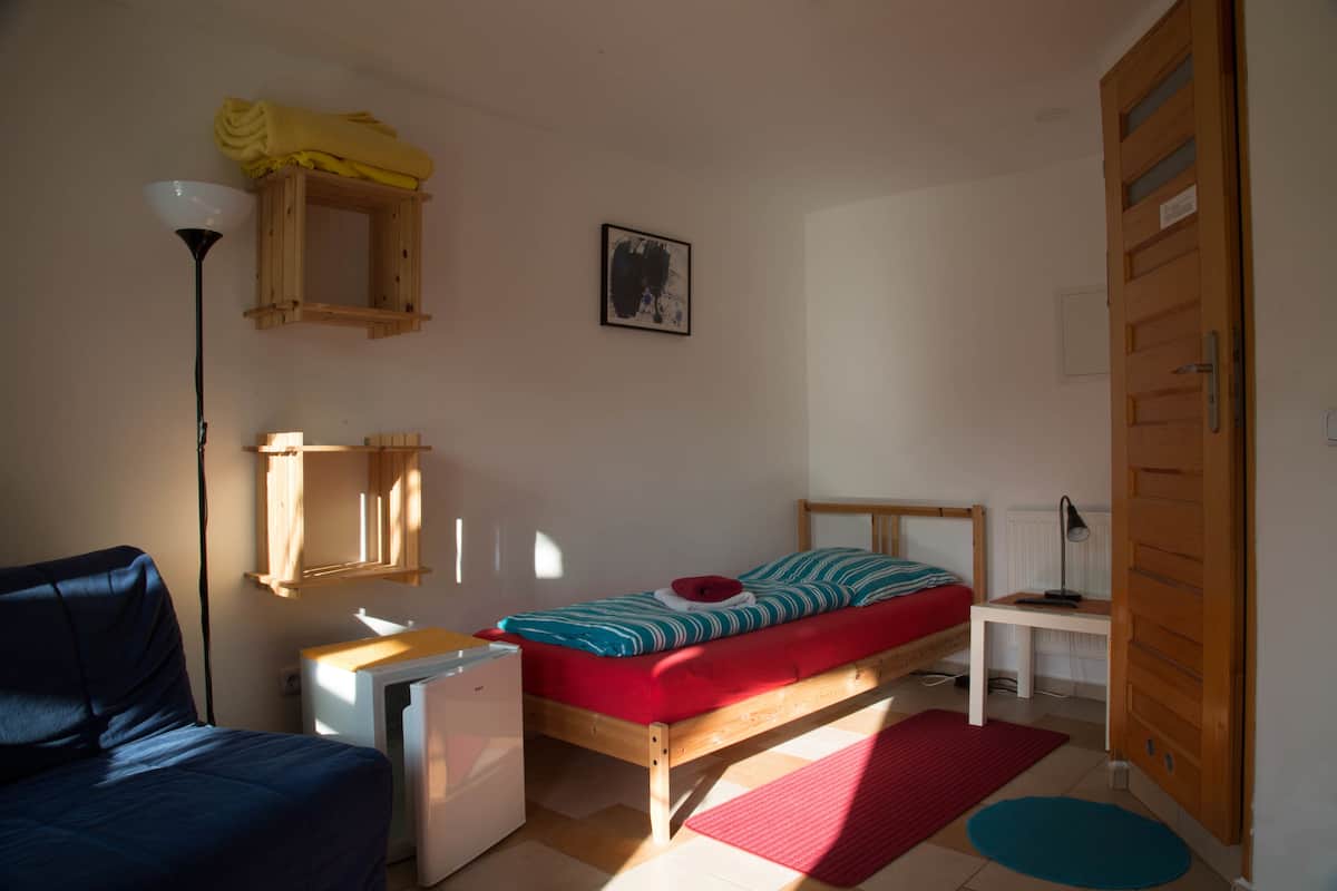 A small, well-lit bedroom with a single bed, a desk, a chair, and a wardrobe.