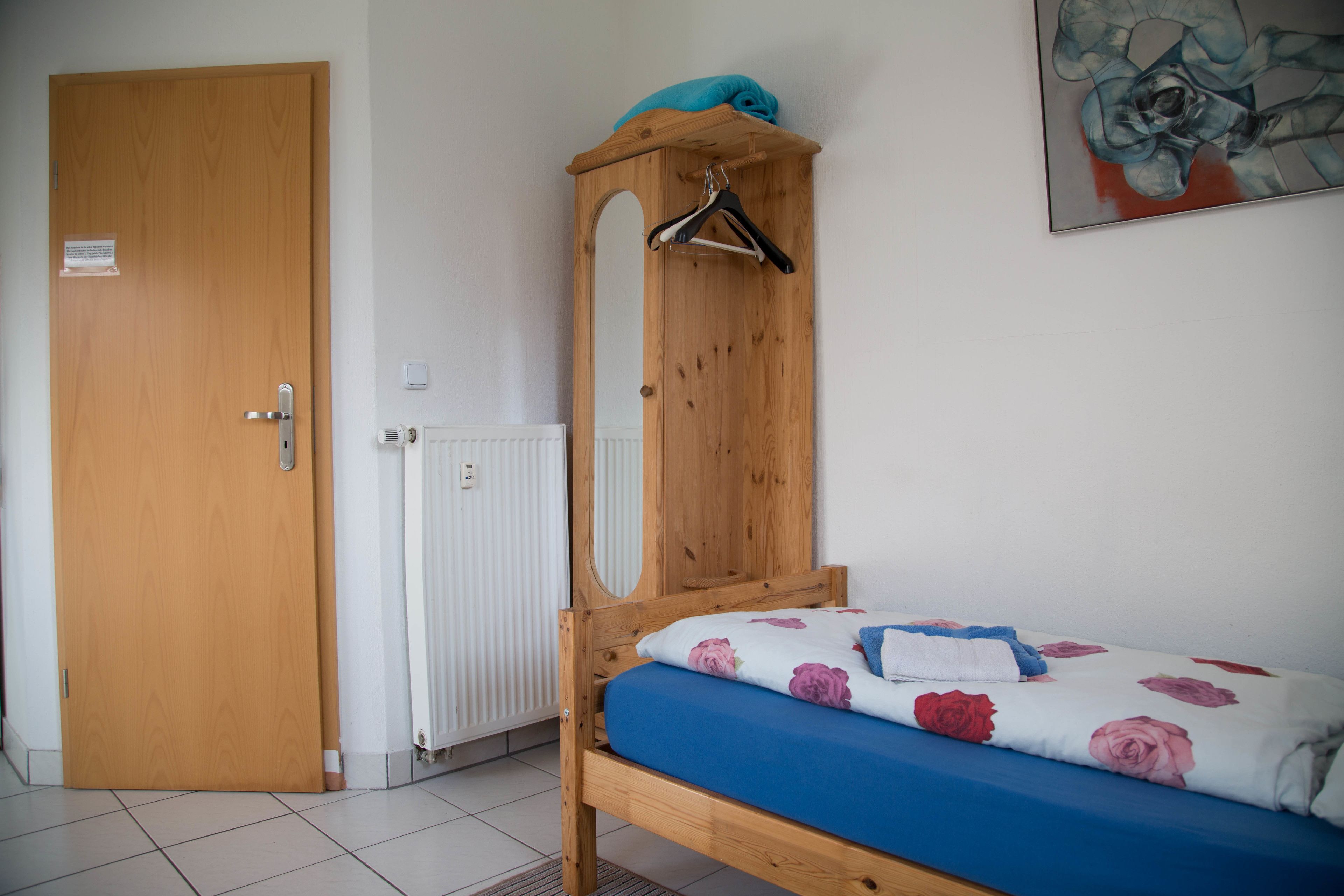 A bedroom with a wooden bed, a hanging clothes rack, a radiator, and a door.