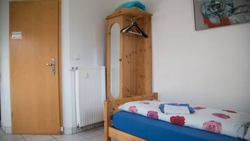 A bedroom with a wooden bed, a hanging clothes rack, a radiator, and a door.