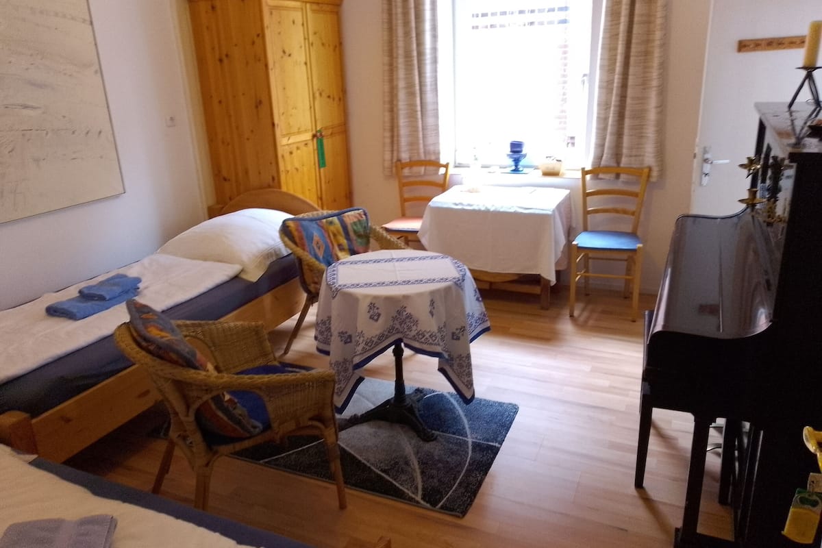 A compact room with a bed, a small table, a chair, a sofa, a cabinet, and a piano.