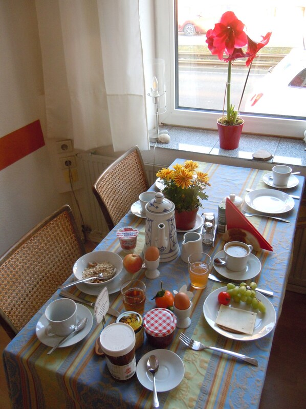 A breakfast table set with various food items and a potted plant by a window.