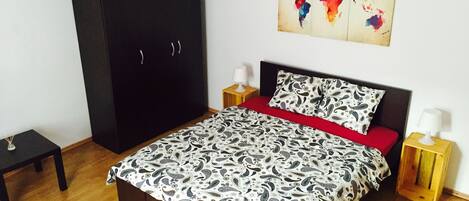 A bedroom with a bed, a wardrobe, a nightstand, a lamp, and a world map on the wall.