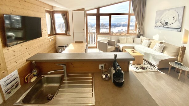 Una cocina moderna con estufa integrada, un ventanal con vistas a un paisaje nevado y una zona de comedor con mesa y sillas de madera.