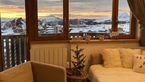 Una habitación acogedora con un amplio ventanal con vistas a un pueblo nevado al atardecer.