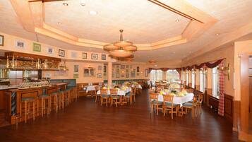 A spacious dining area with wooden tables and chairs, a bar with stools, and framed pictures on the walls.