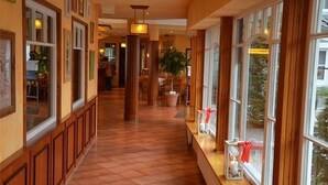 A hotel corridor with wooden paneling, large windows, and a tiled floor. - Ringhotel Kloevensteen (Schenefeld)