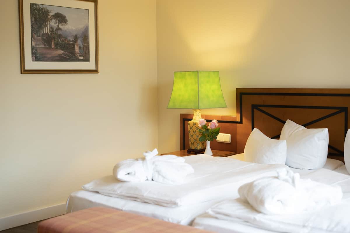 A hotel room with a neatly made bed, a bedside lamp, a vase with flowers, and a framed picture on the wall.