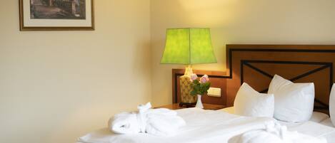 Habitación de hotel con una cama bien hecha, una lámpara de noche, un jarrón con flores y un cuadro en la pared.