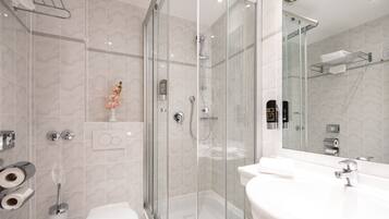 Une salle de bain moderne avec une douche à parois de verre, des toilettes blanches et un grand miroir au-dessus du lavabo.