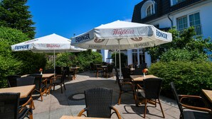 An outdoor seating area with tables and chairs, covered by umbrellas with the brand 'Weißbier' and 'ERDINGER' visible. - Ringhotel Kloevensteen (Schenefeld)
