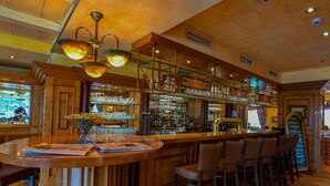 A bar area with wooden bar counters, multiple stools, and a variety of glassware and bottles on shelves. - Ringhotel Kloevensteen (Schenefeld)