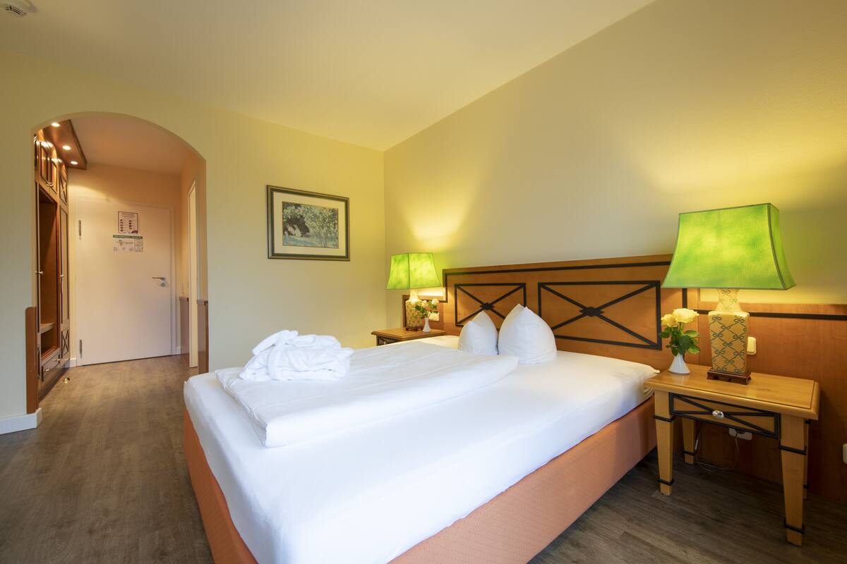 A hotel room with a large bed, two bedside tables with lamps, a wooden headboard, and a framed picture on the wall.