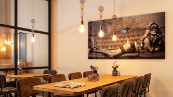 Un comedor con una mesa de madera larga, varias sillas, lámparas colgantes y un cuadro abstracto grande en la pared.