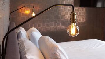 A bed with white linens and gray pillows, a black metal headboard, and a wall with a geometric patterned wallpaper.