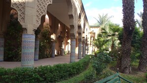 An architectural corridor with arches and columns, surrounded by greenery and a bench. - Riad Jasmeene: Exclusive rental with WiFi and access to Pools!  (Marrakech)