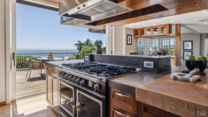 A modern kitchen with a gas stove, wooden cabinets, and a view of the ocean.