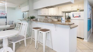 Une cuisine moderne avec des meubles blancs, un comptoir en granit et deux tabourets de bar.