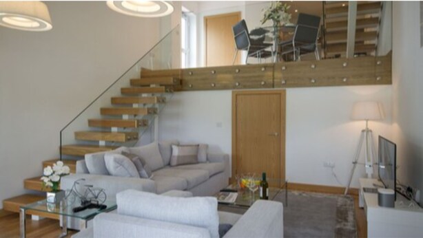 A modern living room with a staircase, a sofa, a coffee table, and a TV. - Tailored Stays  -  Executive Town House (Cambridge)