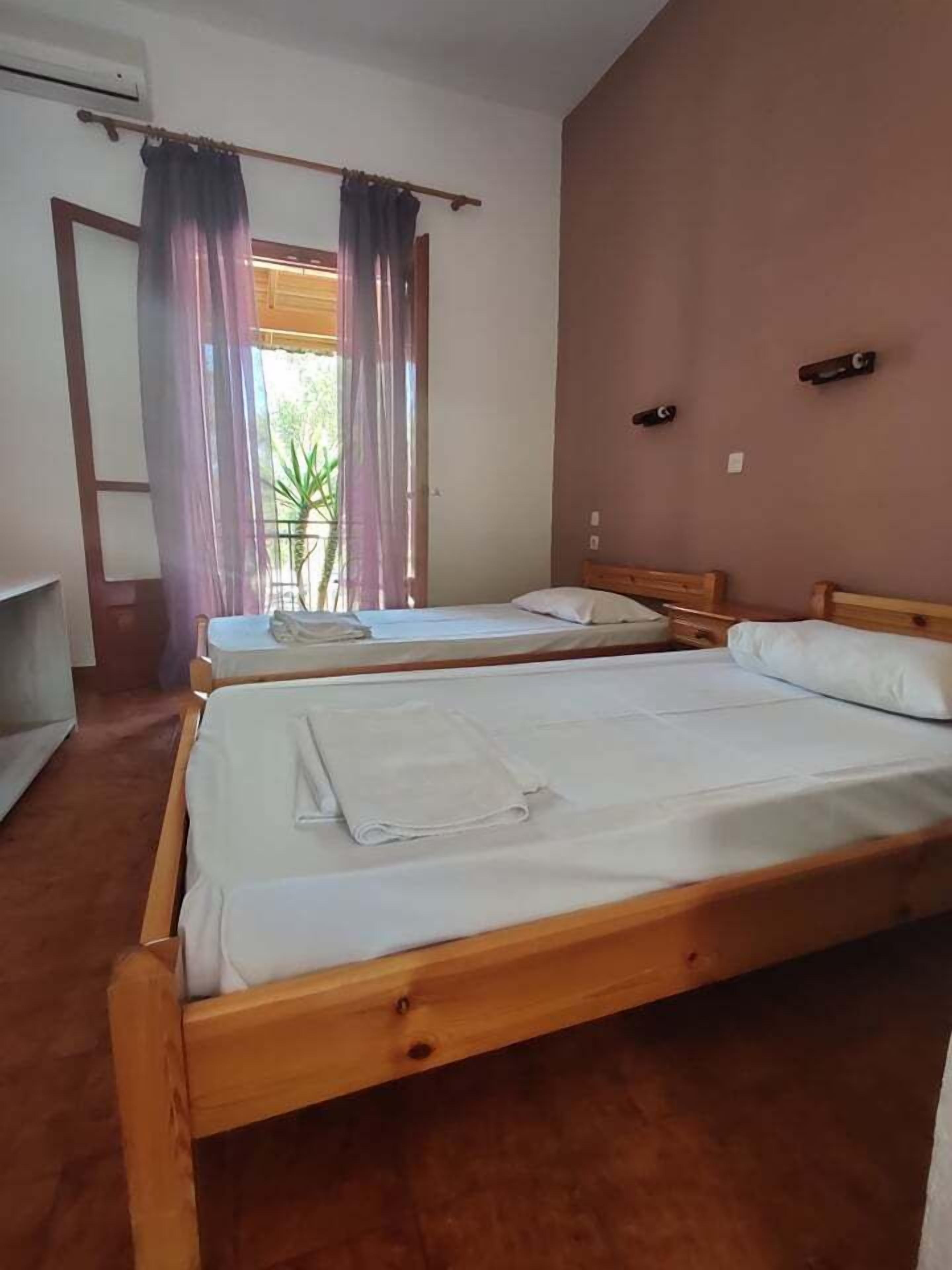 Una habitación con dos camas de madera, una ventana con cortinas y una puerta.